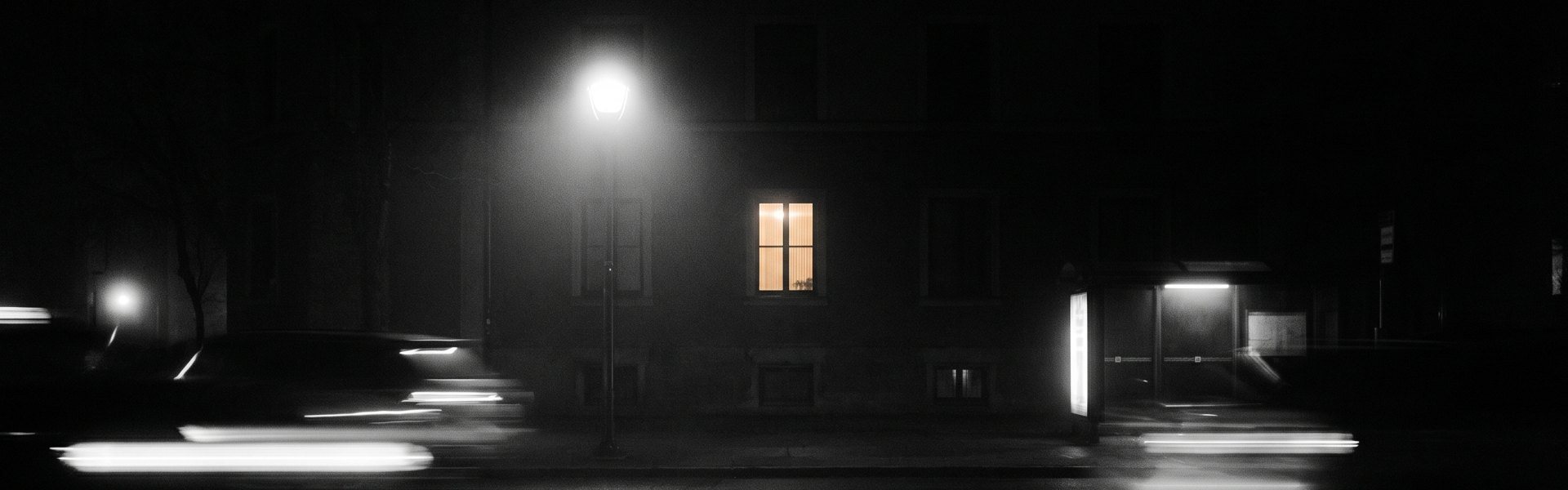 A black and white photograph of a wet city street at night, reflecting blurred lights from a streetlamp and a distant window -- adcreative ai alternatives top a