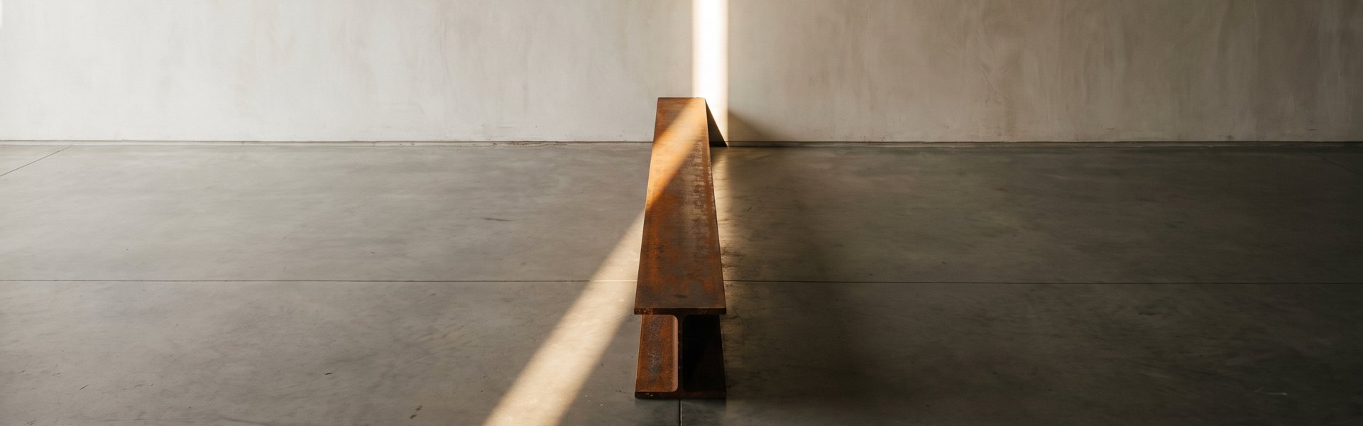 A blade of sunlight illuminates an oxidized steel threshold on a concrete floor next to a plaster wall. -- AI ad creative benchmarks by vertical 2026