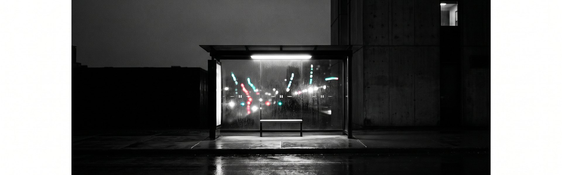 Wet street reflecting a bus shelter's light at night, surrounded by dark buildings and sky -- heygen alternatives top ai creative options in 2026