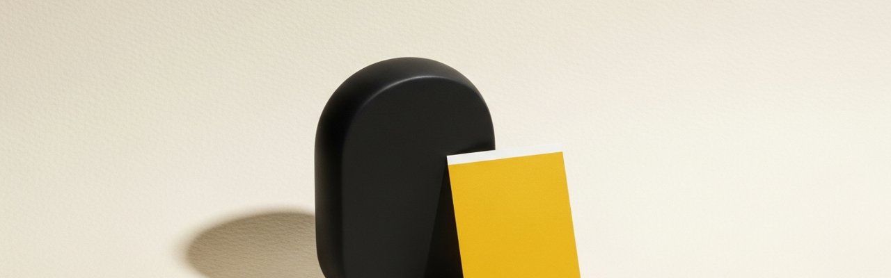 Black abstract object beside a yellow paper swatch on cream surface — performance creative agency.