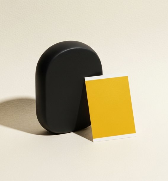 Black abstract object beside a yellow paper swatch on cream surface — performance creative agency.
