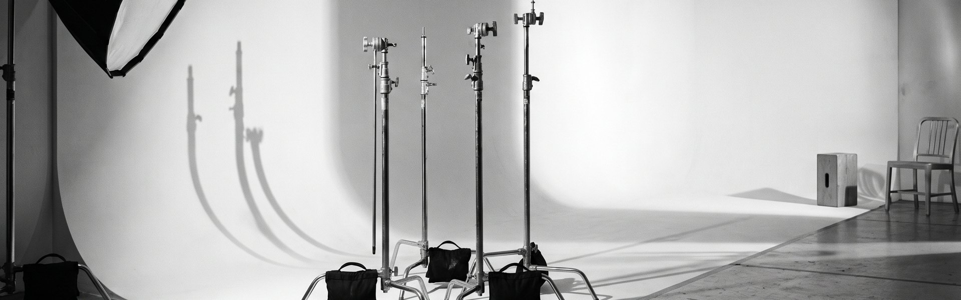 Three C-stands with sandbags cast long shadows on a white cyclorama floor under a softbox light. -- sora vs veo vs kling
