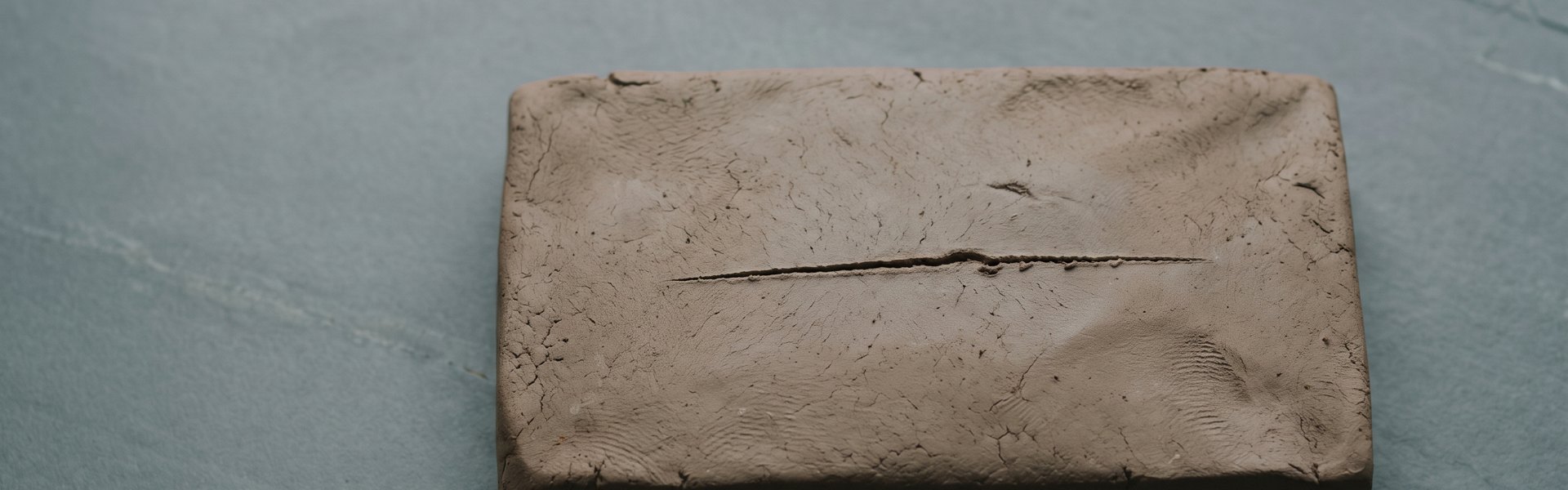 A rectangular block of unfired clay with a score line rests on a grey slate surface. -- subscription app creative strategy